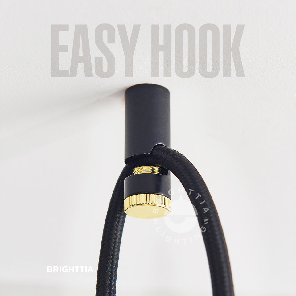 Brighttia Easy Hook in black & gold mounted on white ceiling with a black fabric cord hanging on it.