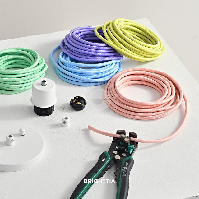 Making a white pendant light fixture with light color fabric cords on white surface. A wire stripper stripping a pink fabric cord.