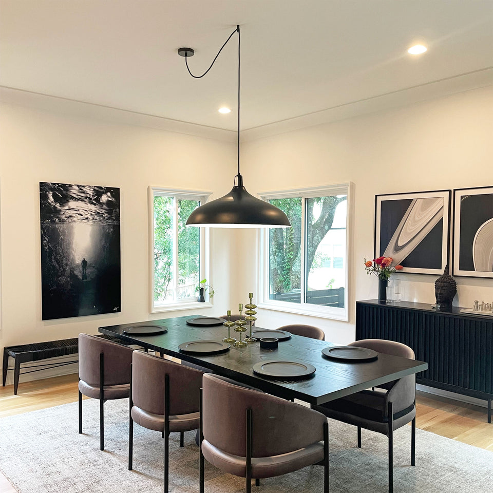 Large black shade pendant light swag to center of black dining table using a black easy ceiling hook XL in spacious and bright dining room with black and white art work hanging on wall.