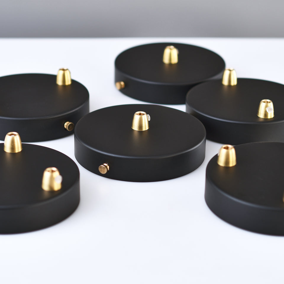 A group of black ceiling canopies with cone-shaped brass cord grips and thumbscrews displayed on table.