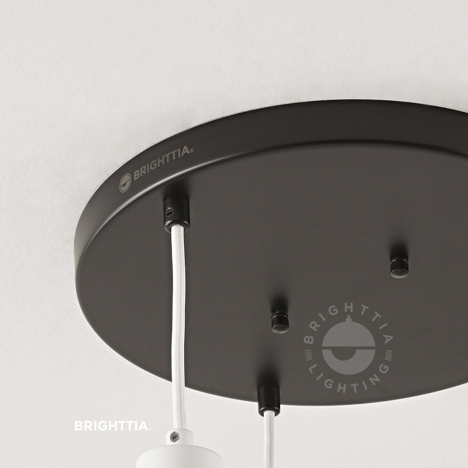 Close up view of laser etched BRIGHTTIA logo on 12in black 3-port ceiling canopy with black cord grips mounted on white ceiling. 