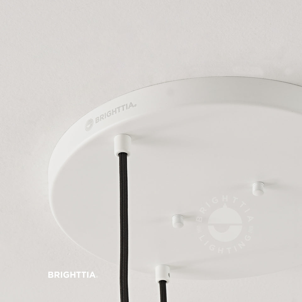 Close up view of laser etched BRIGHTTIA logo on 12in white 3-port ceiling canopy with white cord grips mounted on white ceiling. 