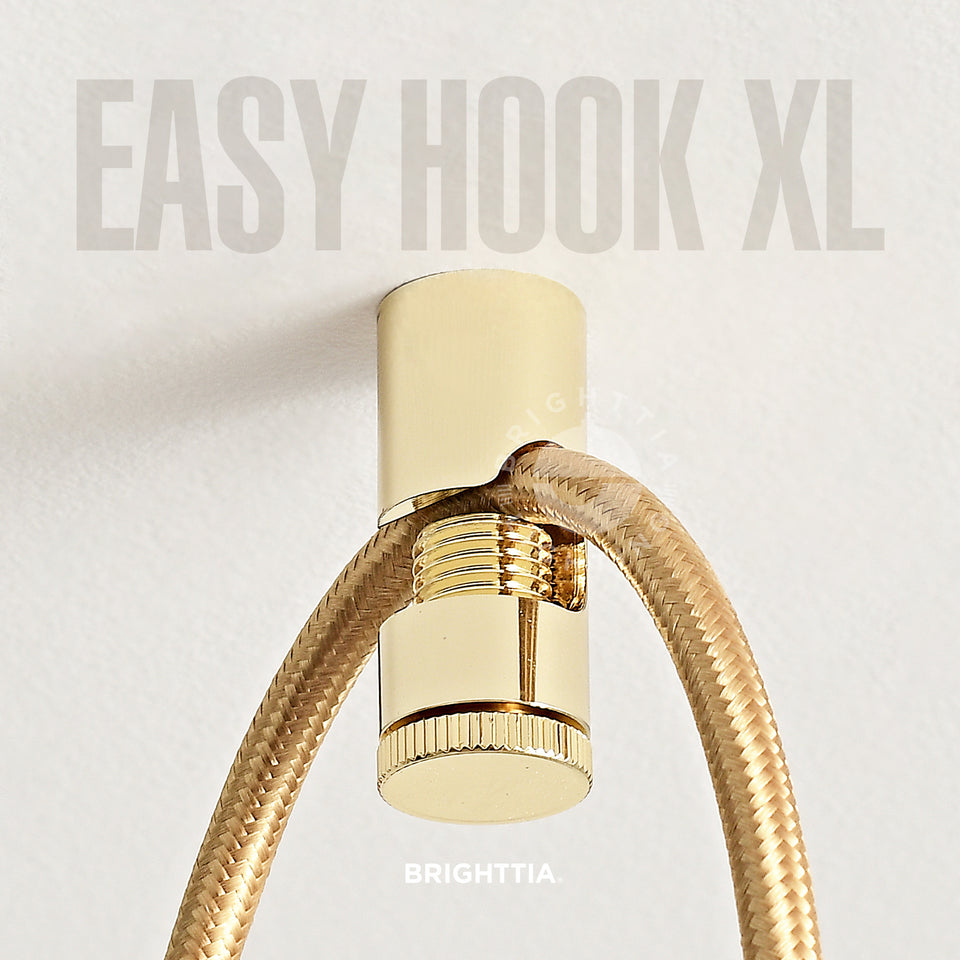 A gold easy hook XL mounted on white ceiling with a brass fabric cord hanging on it.