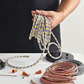 Hand holding a roll of rainbow color fabric cord making a DIY pendant light fixture on a white surface.